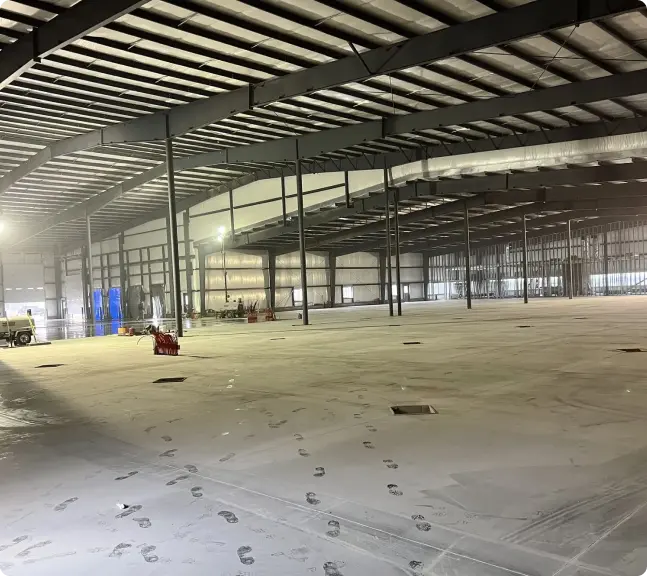 Interior of a large, empty warehouse with a newly poured concrete floor and visible footprints.