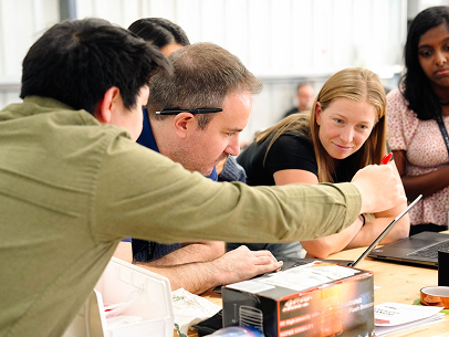A group of people are crowding around a table and looking at something on a laptop screen