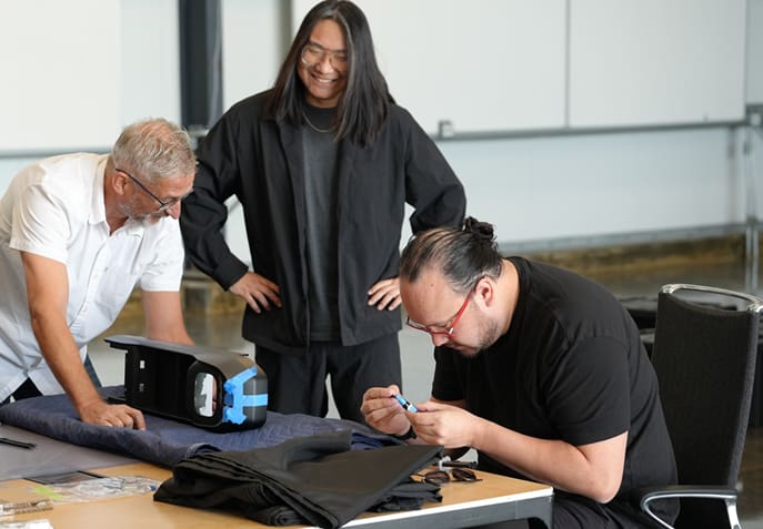 Three men are working on small parts on a table