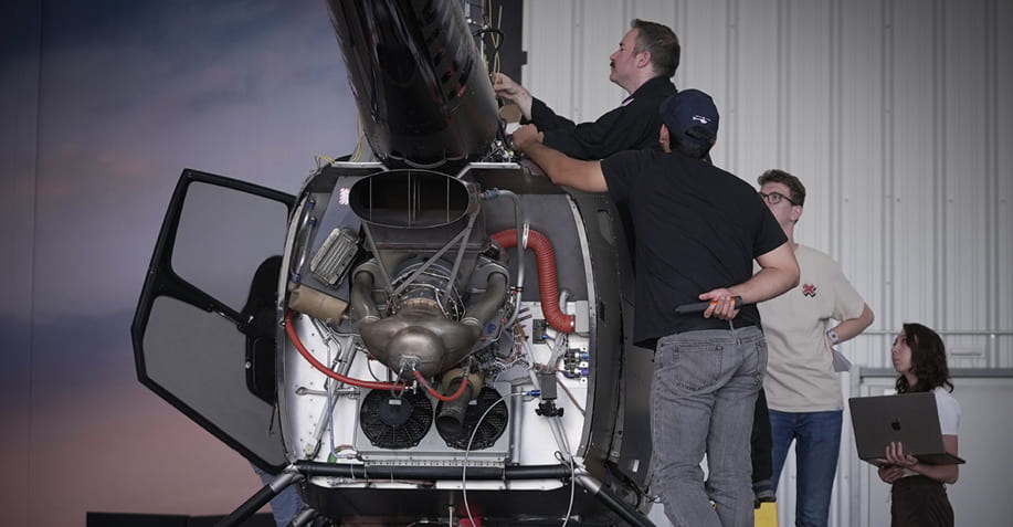 A group of people is standing around and working on the top part of the helicopter