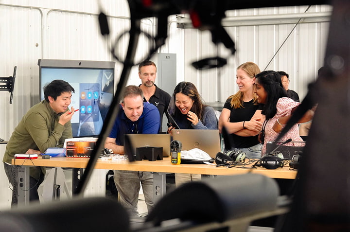 A team is meeting around a table laughing at something on a laptop screen