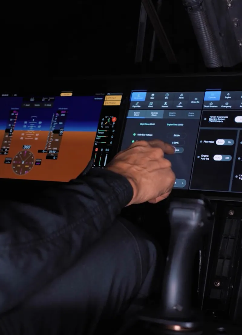 Person operating a touchscreen control panel inside an aircraft cockpit with flight instruments displayed.