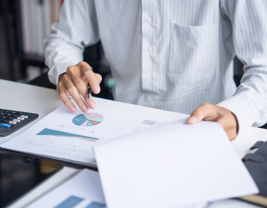 Person seated at a desk reviewing a printed report with charts and graphs and using a calculator, illustrating the importance of auditable, high-quality carbon emissions data.