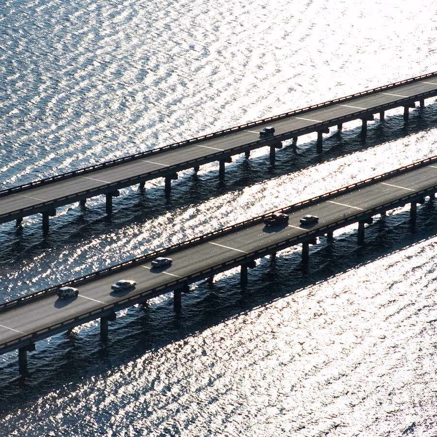 Overhead view of twin highways spanning bright water, evoking Agulhas FS’s commitment to direction, stability, and efficient pathways in fund services.
