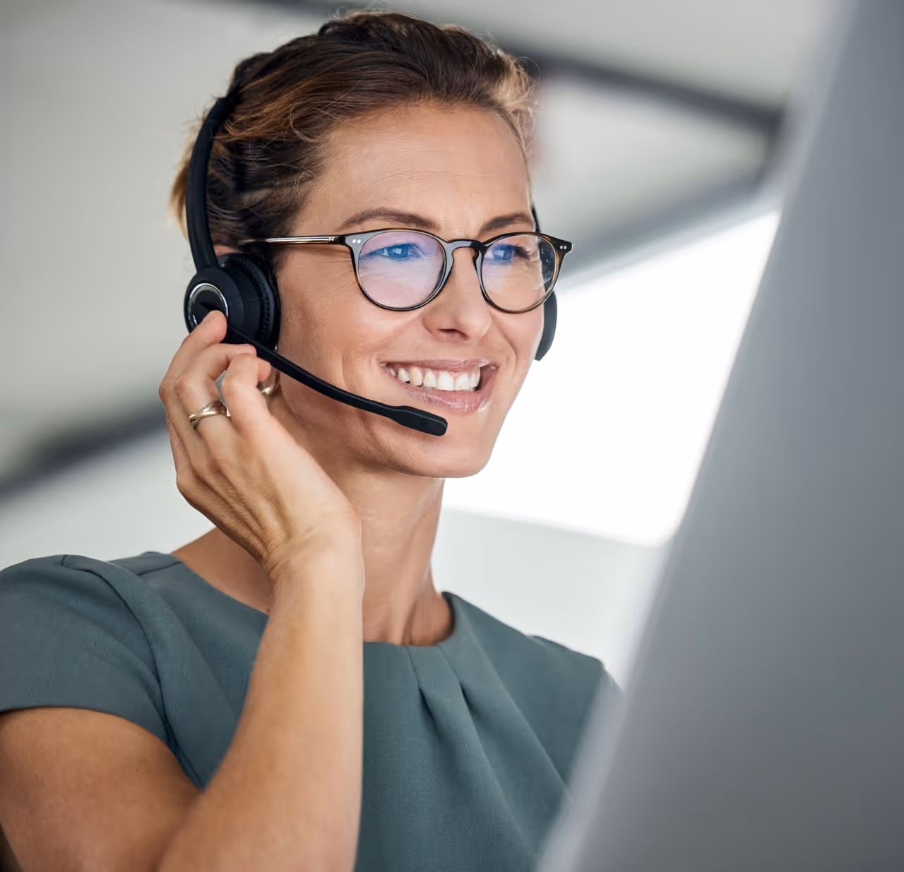 Frau die vor einem Computerbildschirm sitzt und in ein Headset spricht