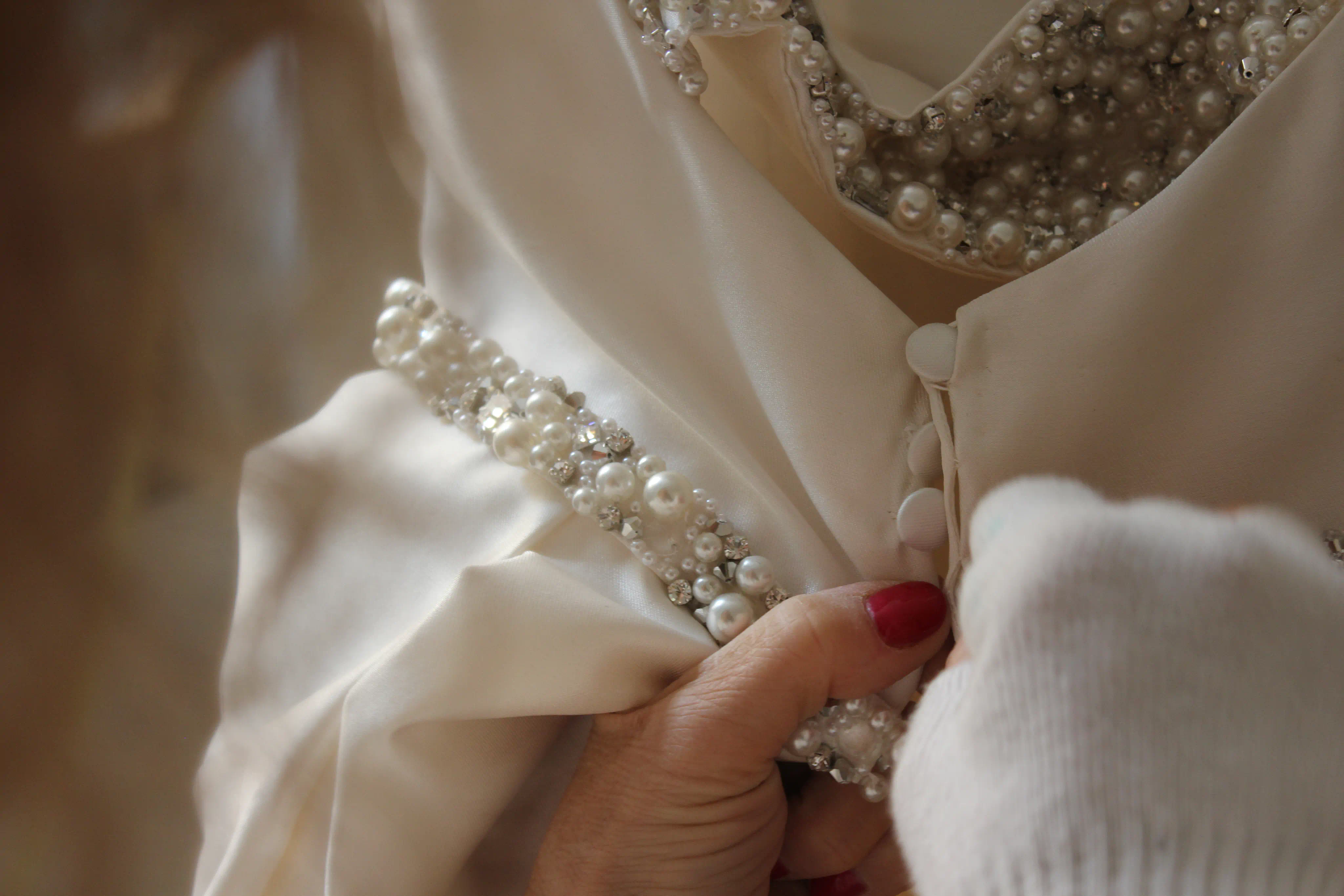 Close-up of an André Laug bridal gown in ivory satin, featuring pearl and crystal embellishments and covered buttons.