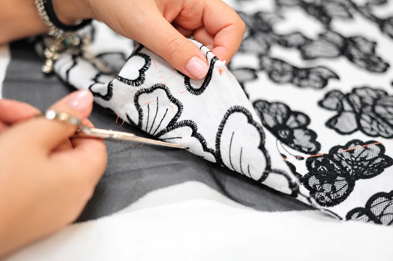 Close-up of hands trimming threads from black floral embroidery on white fabric in the André Laug atelier.