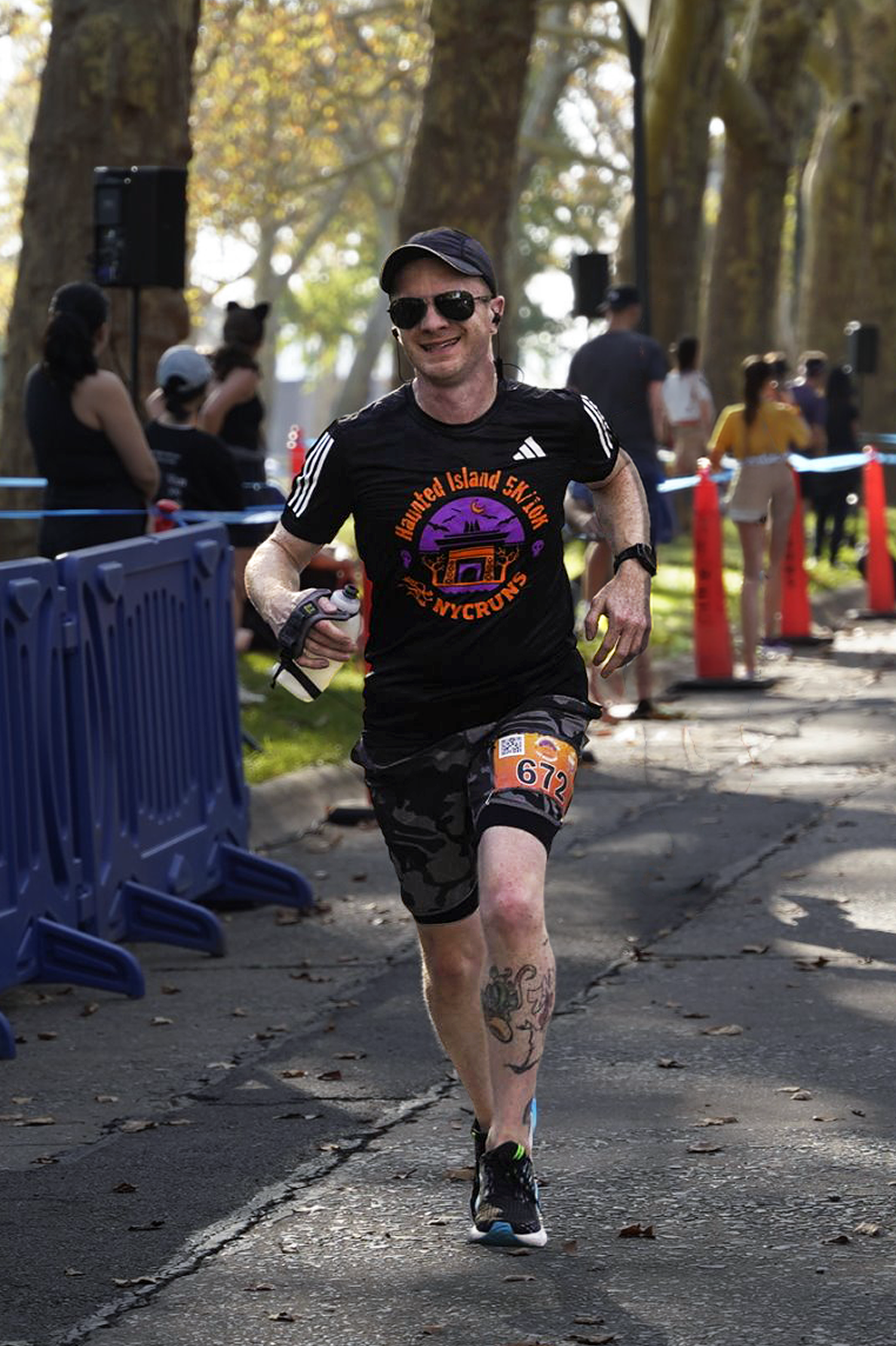 Male runner smiling mid-stride in a race wearing sunglasses, black cap, and Haunted Island 5K shirt.