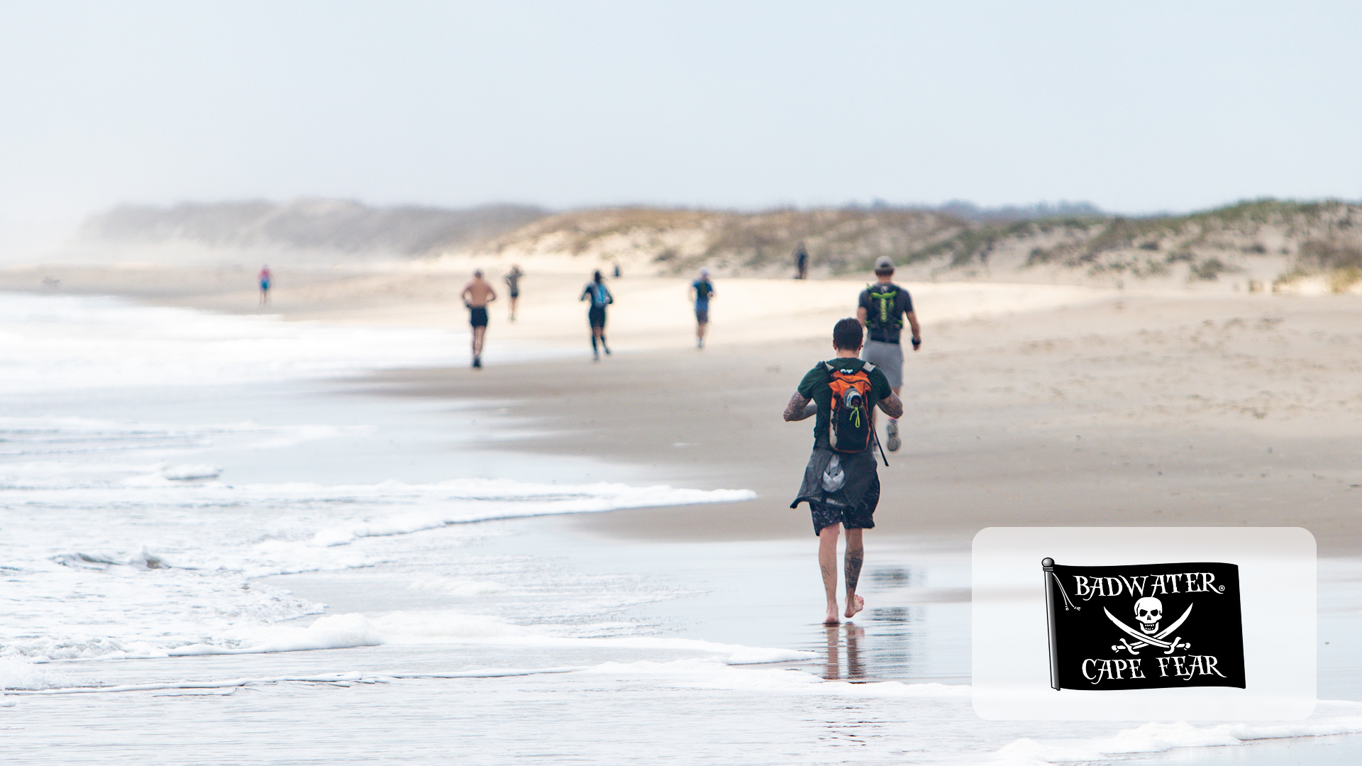 People walking and running along a sandy beach near the ocean under a clear sky.