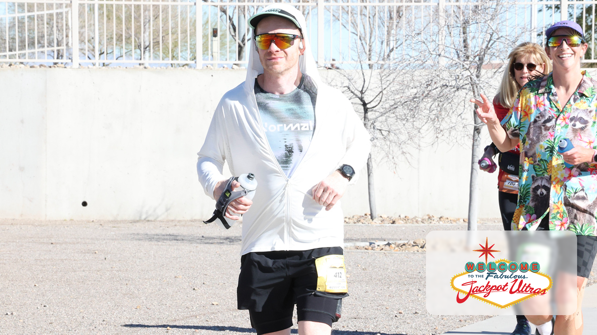 Runners in colorful gear jogging outdoors on a sunny day with leafless trees and a concrete wall background.