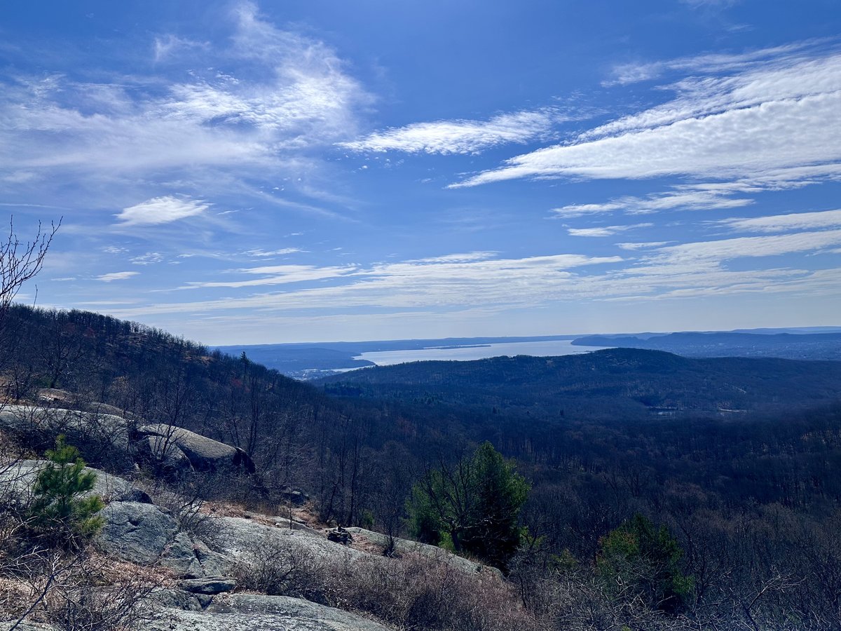 Panoramic view from the West Mountain ridge, Hudson River stretching into the distance below rolling forested hills under a blue sky with high clouds