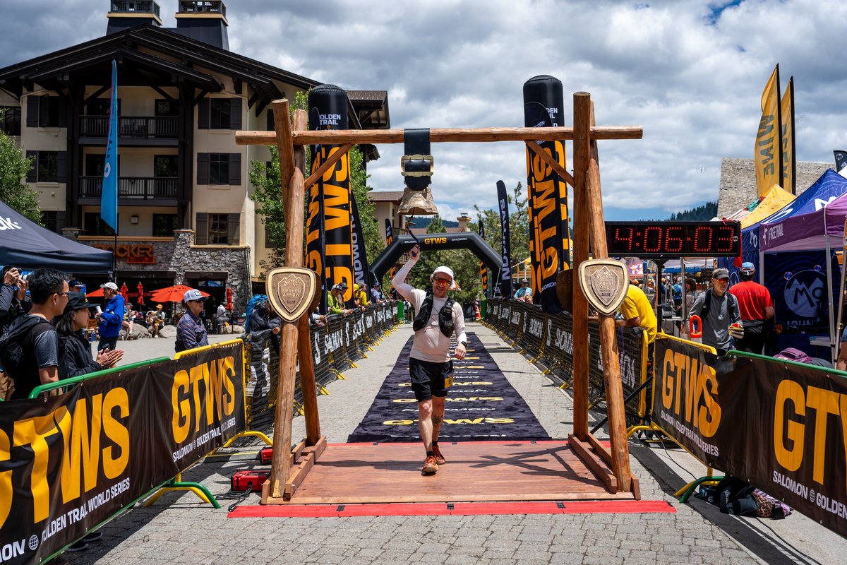Crossing the finish line at Palisades Tahoe Village, one arm raised, bib visible, the GTWS finish arch overhead and the clock showing 4:06:05