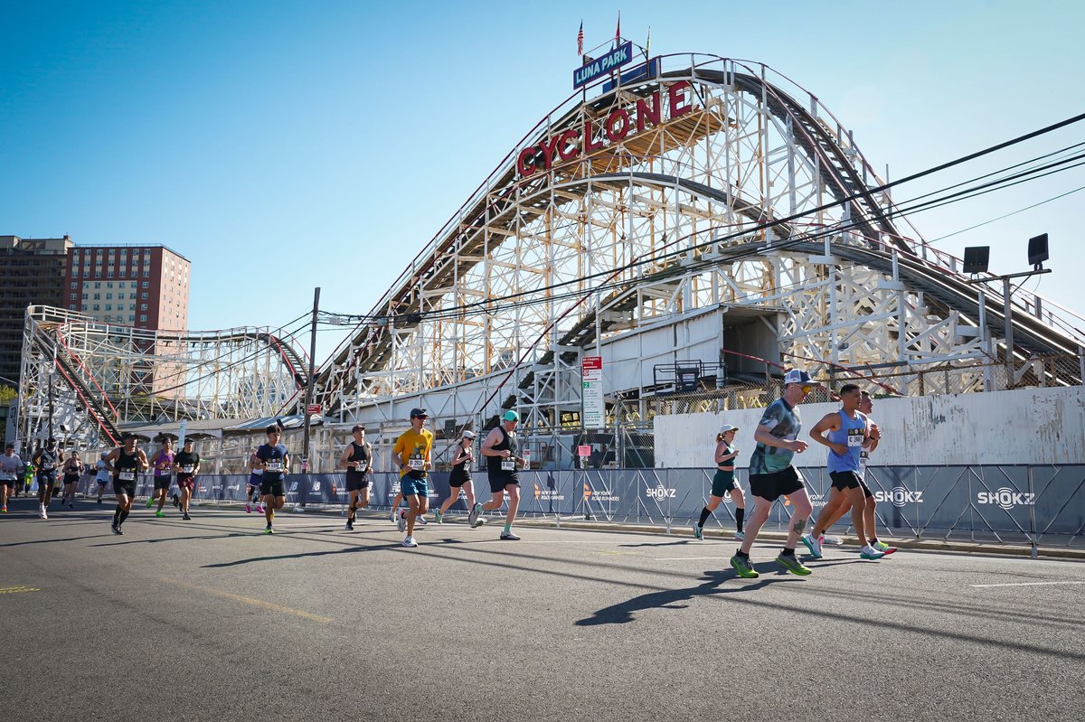 Runners passing beneath the Cyclone roller coaster at Coney Island's Luna Park on a clear blue-sky morning