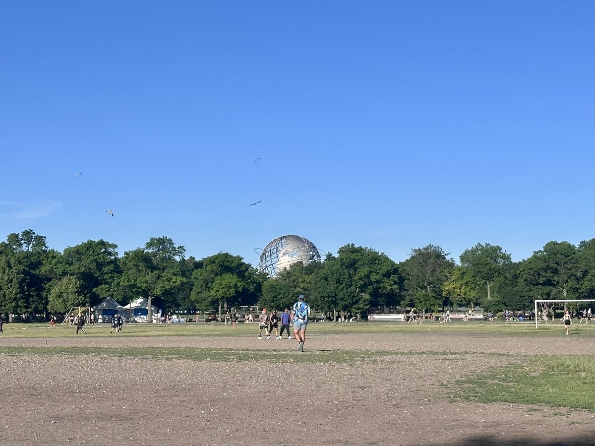 The Unisphere visible across the open fields of Flushing Meadows before the race, soccer games already underway