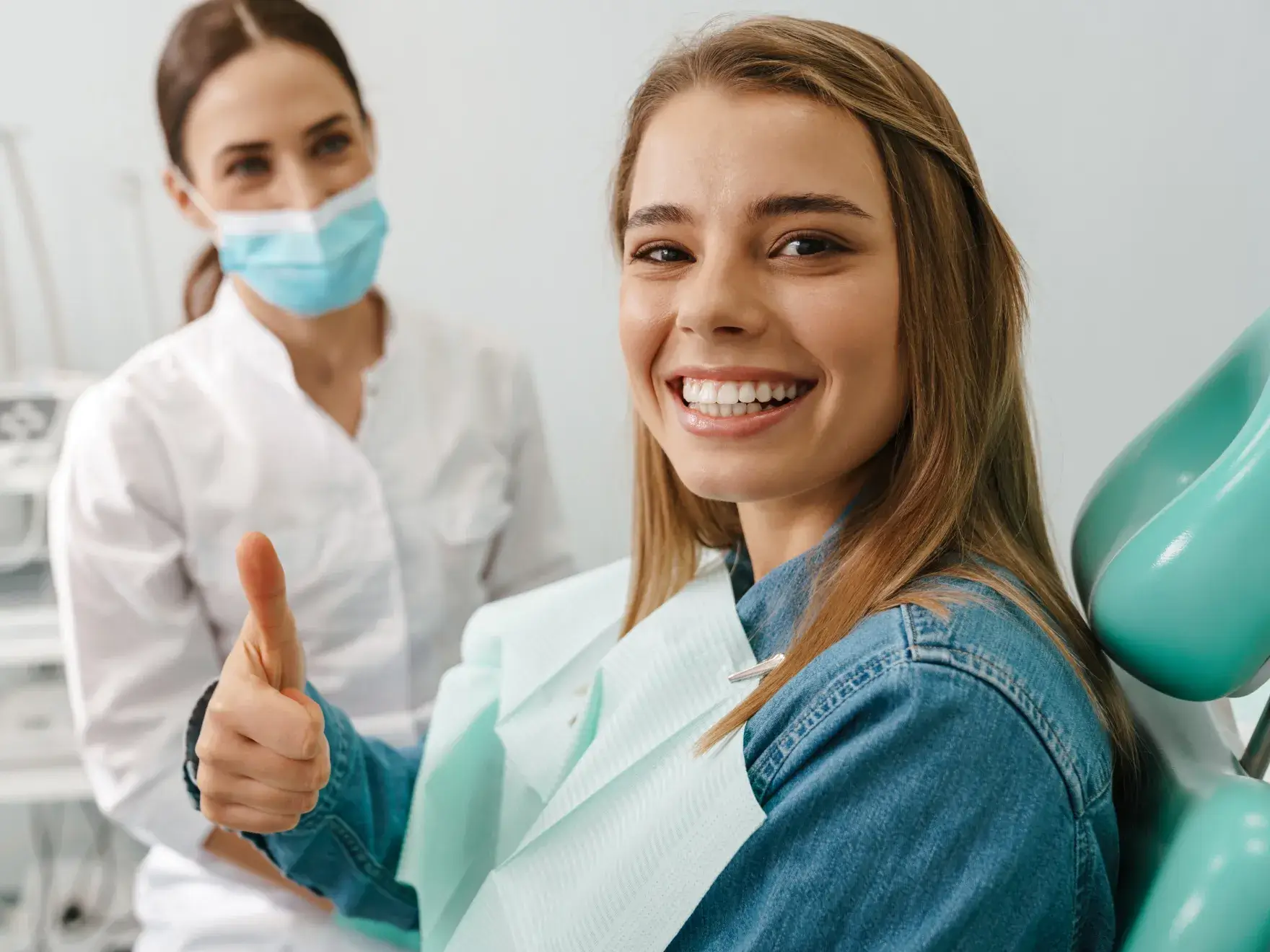 A woman in a dentist's office giving a thumbs up.