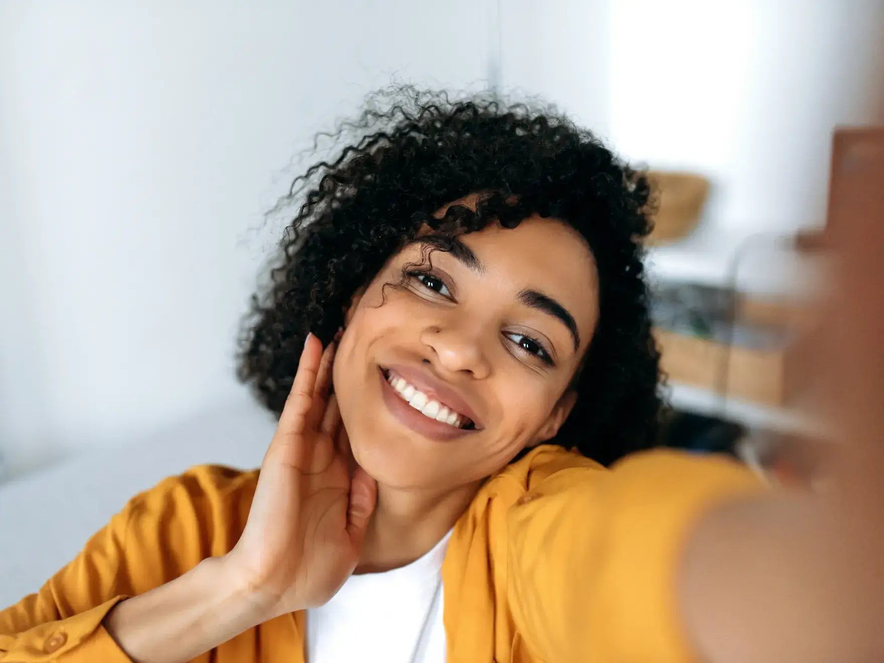 A woman smiling and holding her hand to her ear.