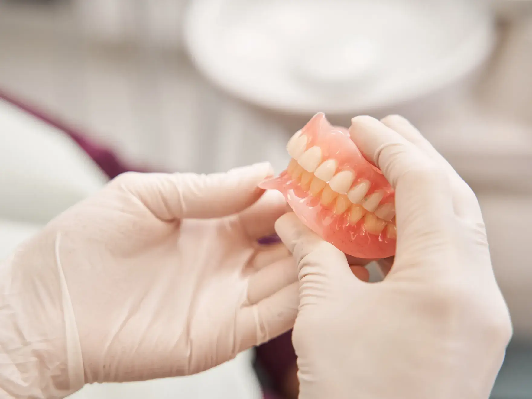 A person in white gloves holding a fake tooth.