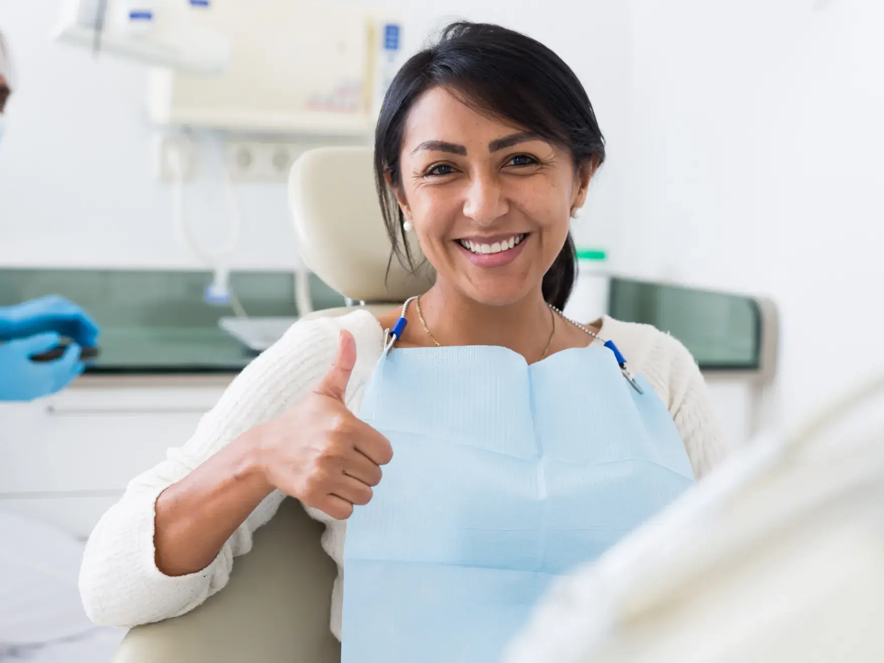 A woman in a dentist chair giving a thumbs up.