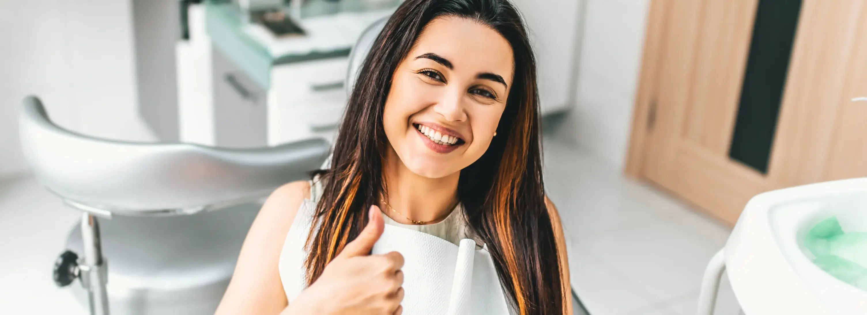 A woman giving a thumbs up in a dental office.