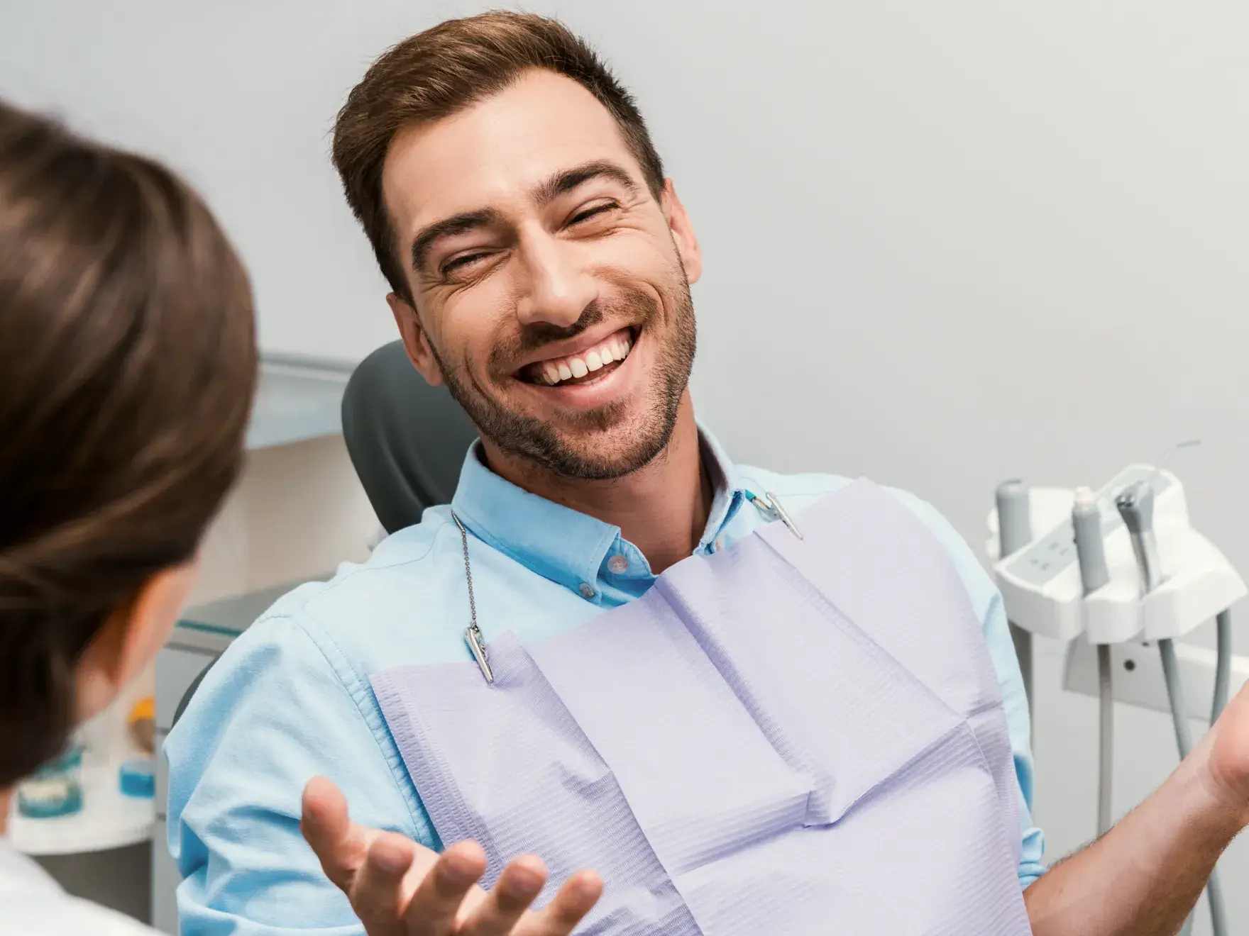 A smiling man in a dental chair talking to a woman.