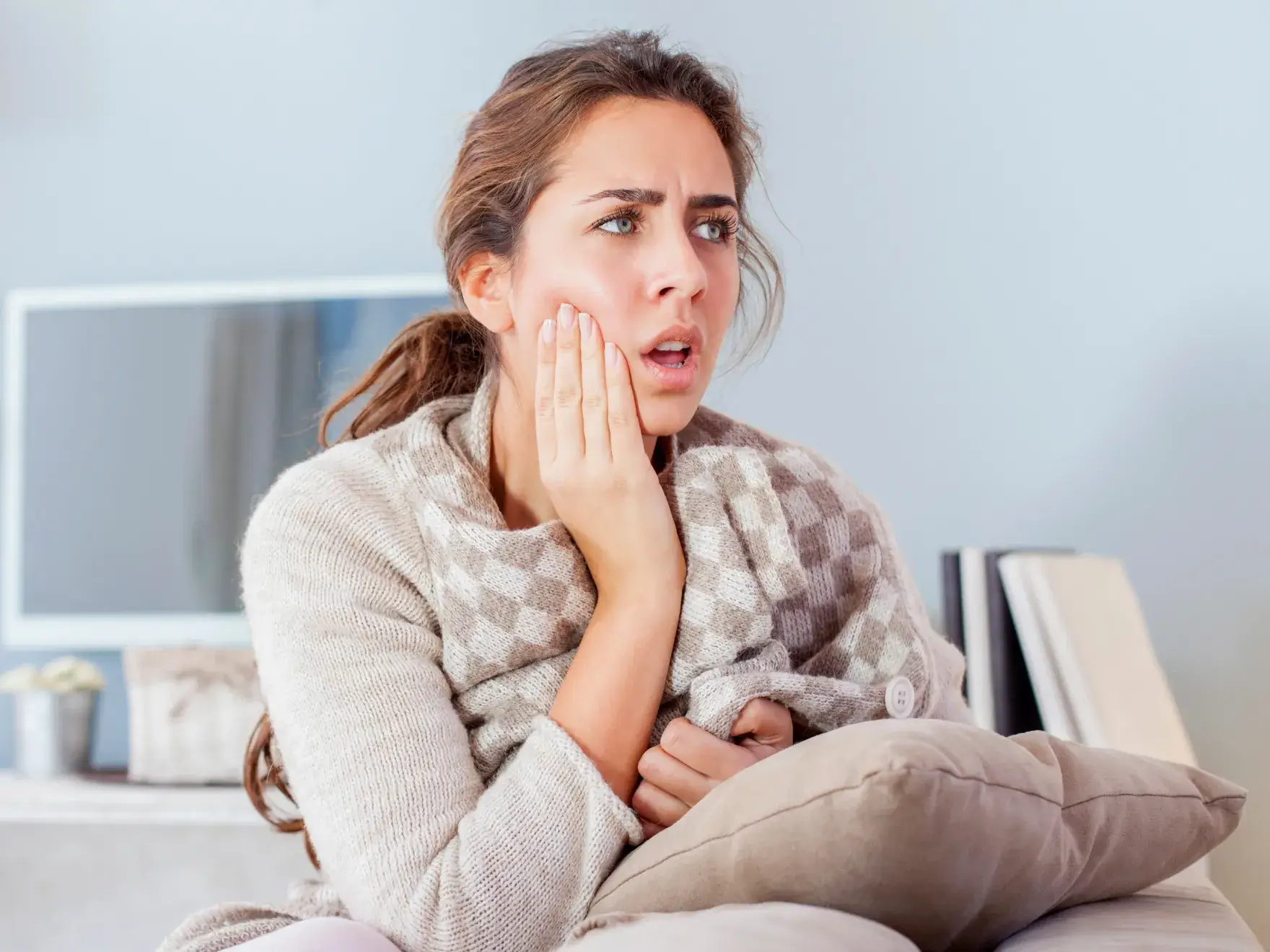 A woman sitting on a couch holding her hand to her face.