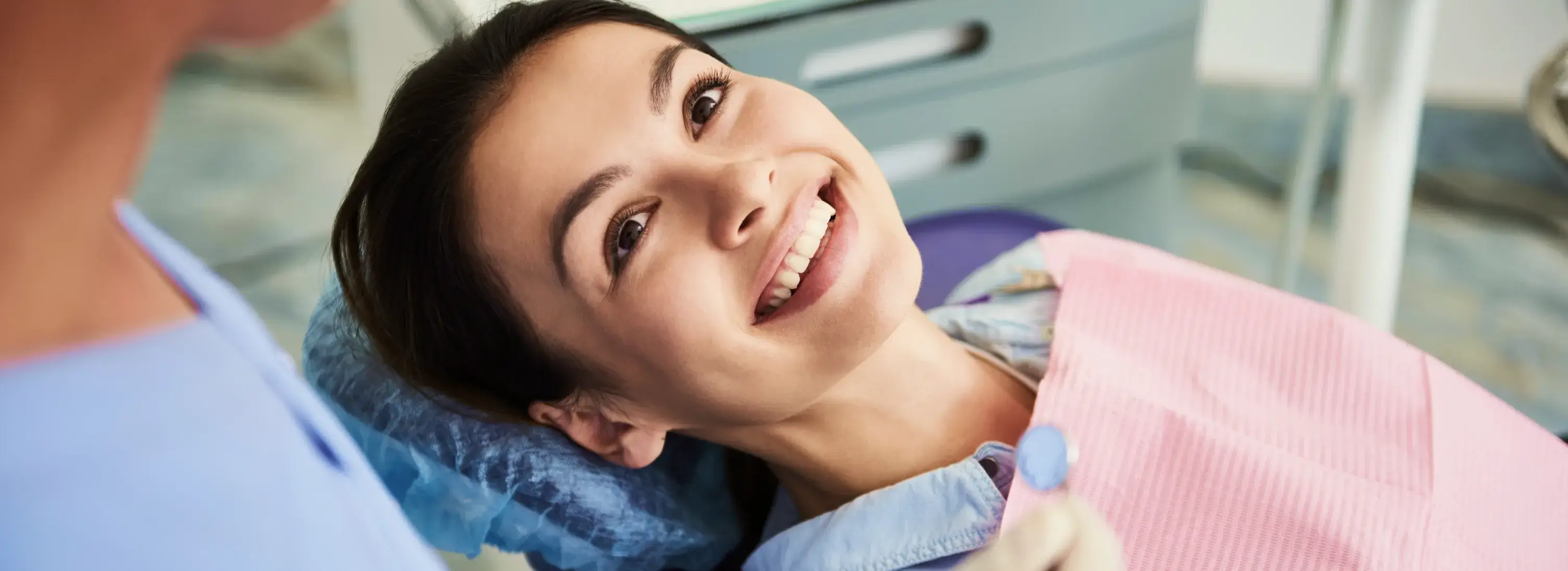 A woman is smiling as she sits in a dentist chair.