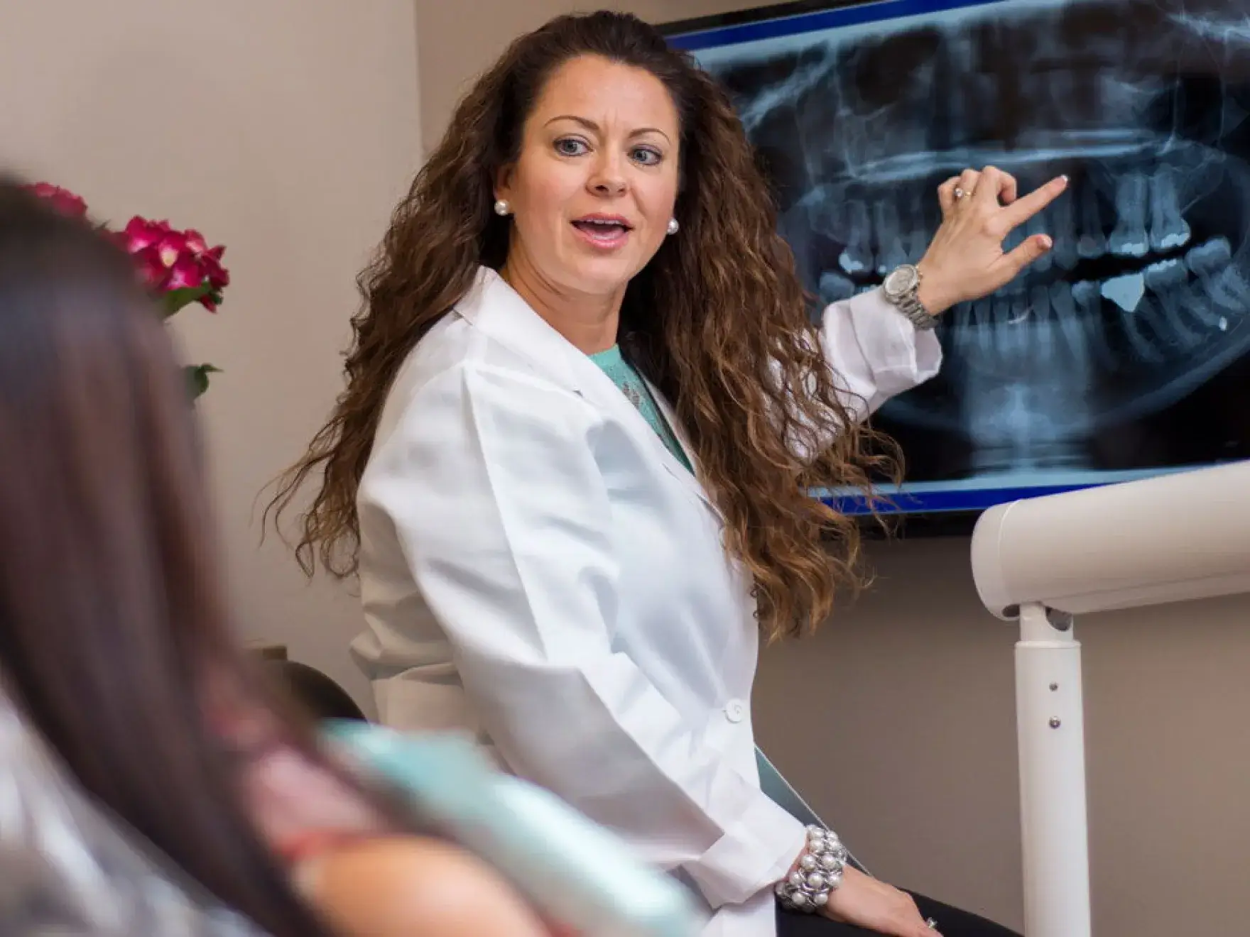 A woman in a white lab coat pointing to a x - ray.