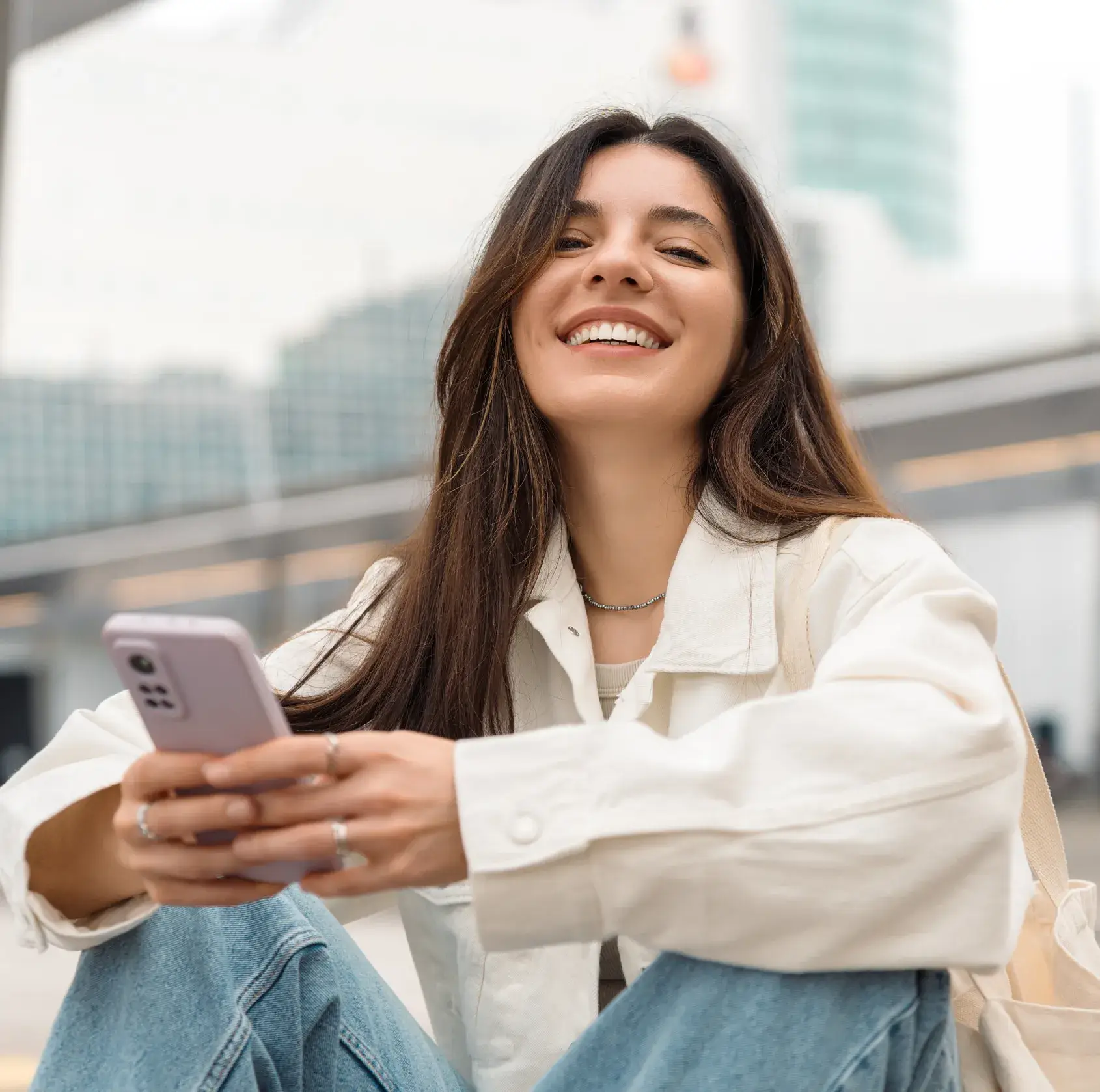 A woman sitting on the ground looking at her cell phone.