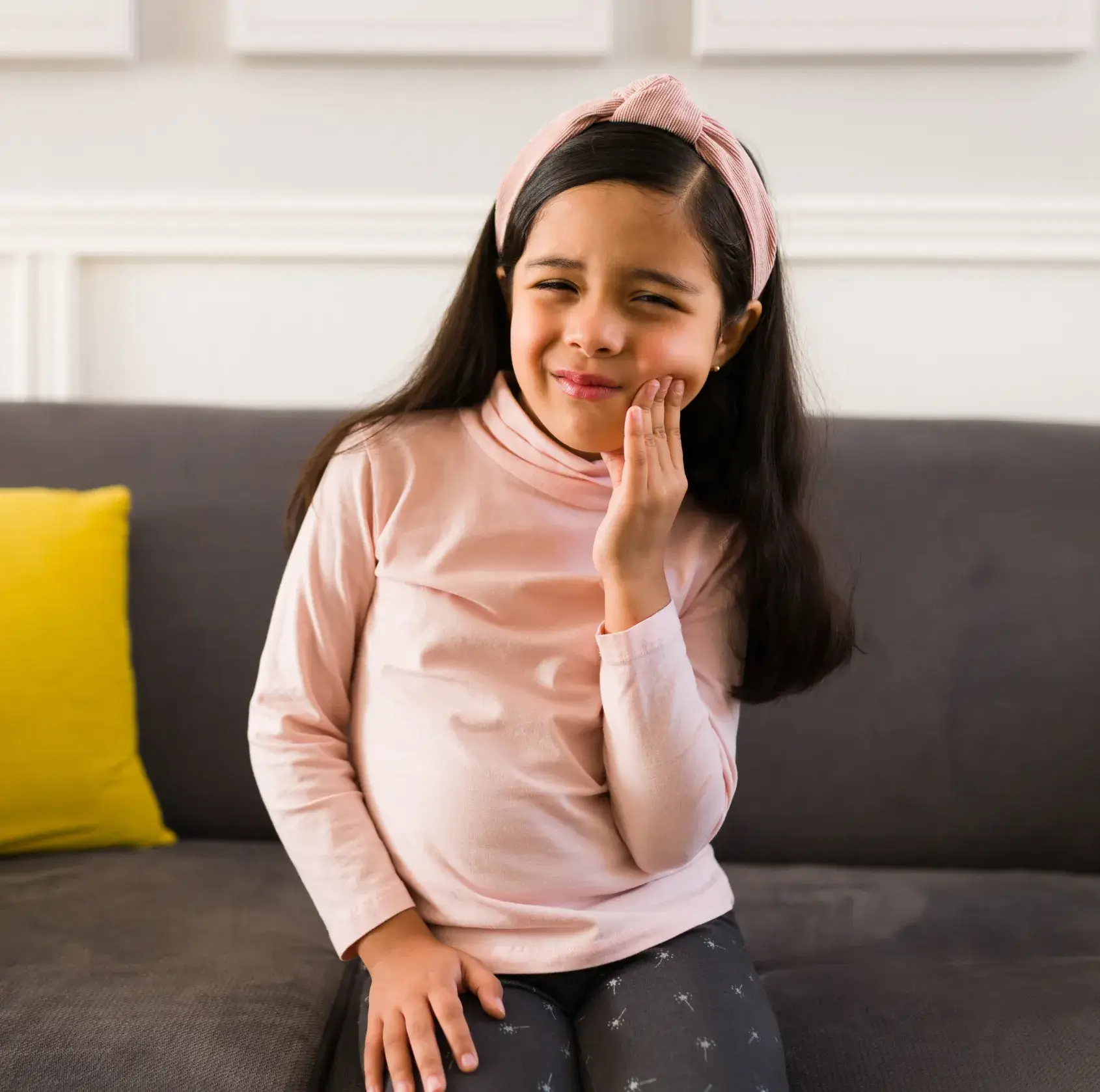 A little girl sitting on a couch with her hand on her face.