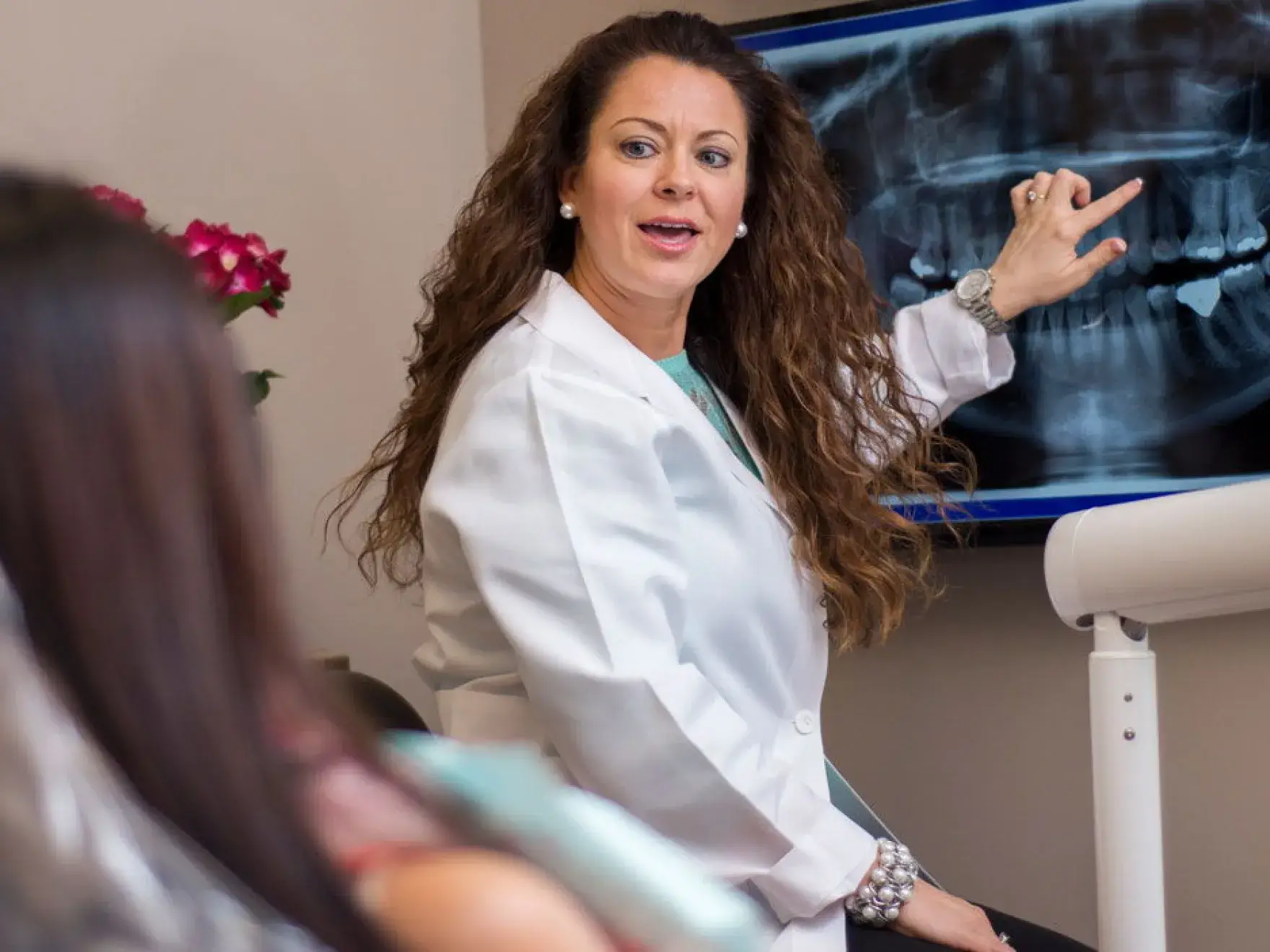 A woman in a white lab coat pointing to a x - ray.