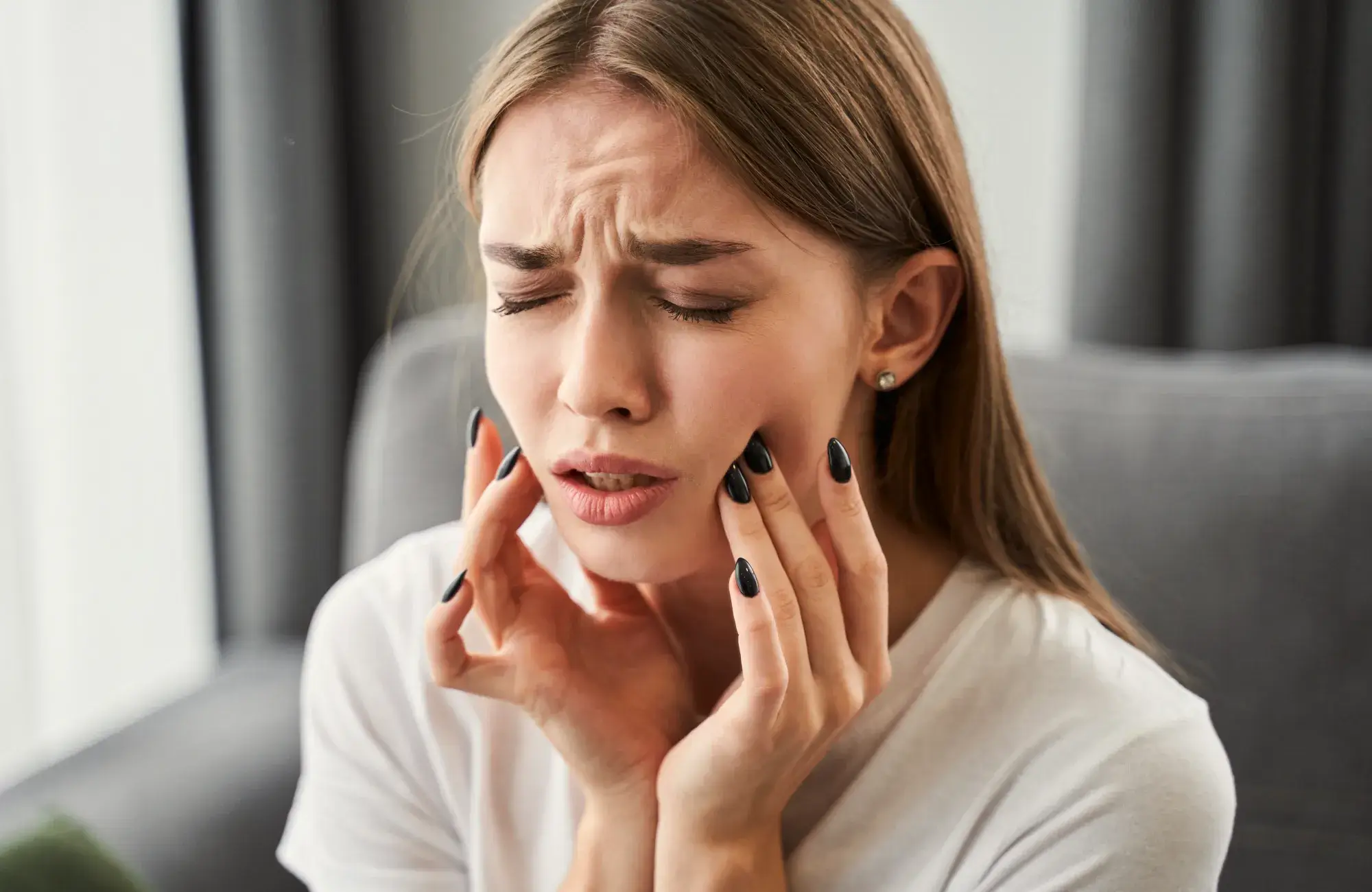 A woman sitting on a couch holding her hands to her face.