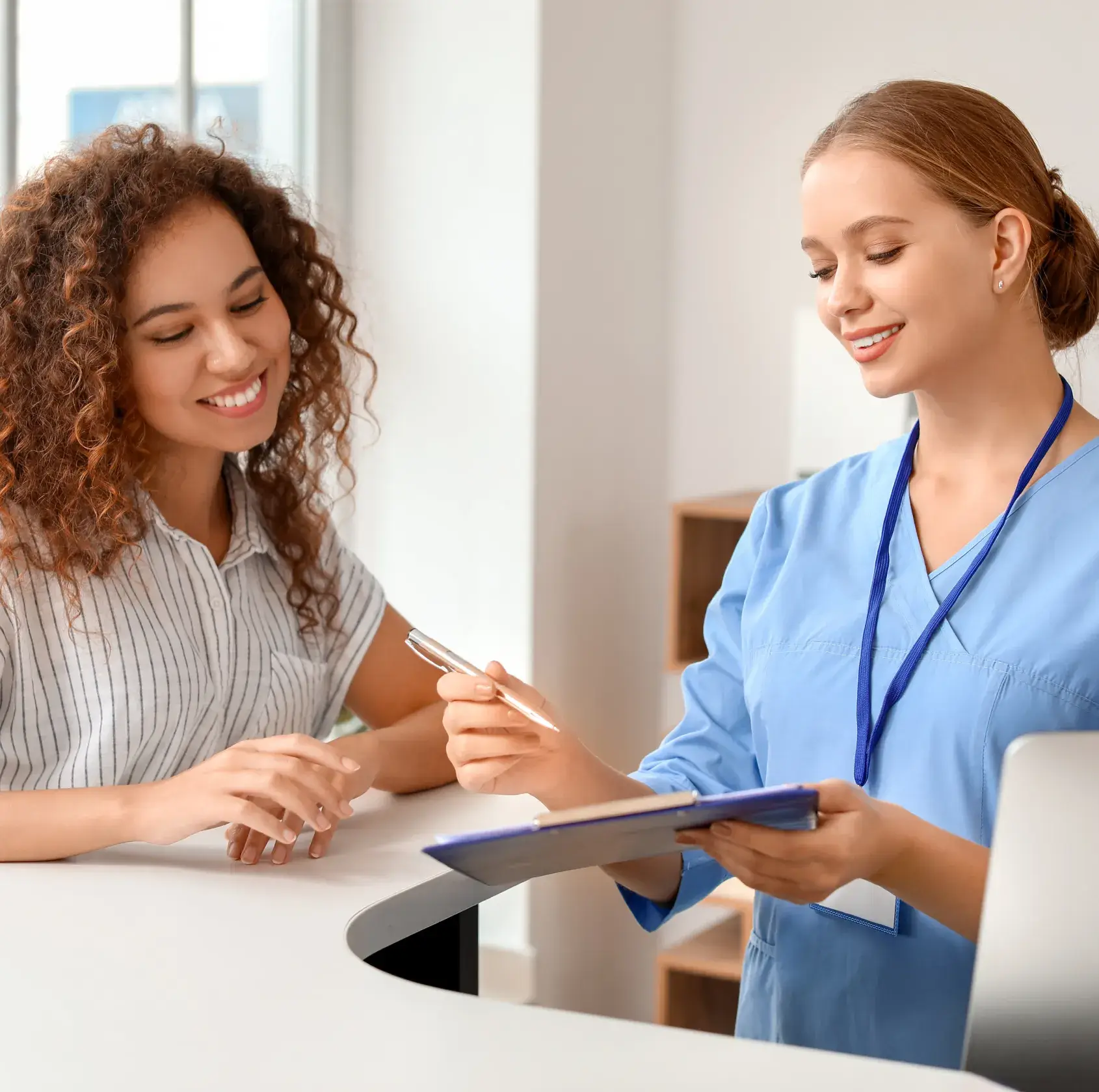 Two women in scrubs are sitting at a desk.