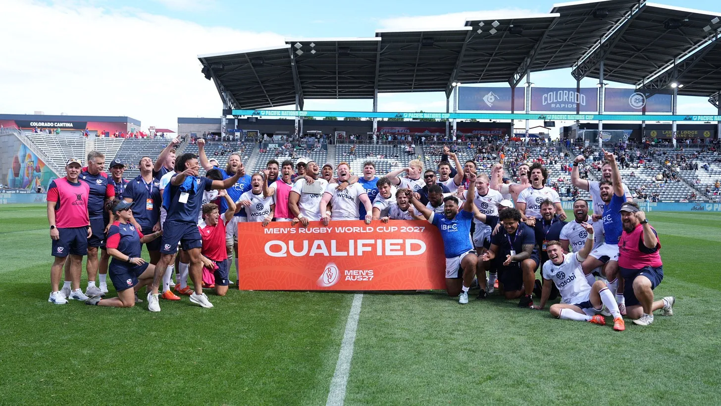 A large group of rugby players and team staff celebrate on a field in front of a banner reading "MEN'S RUGBY WORLD CUP 2027 QUALIFIED," marking their achievement of qualifying for the 2027 tournament. The stadium signage indicates the location is home to the Colorado Rapids.