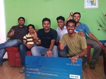 Freshworks founders Girish Mathrubootham and Shan Krishnasamy holding a donation check alongside their first employees