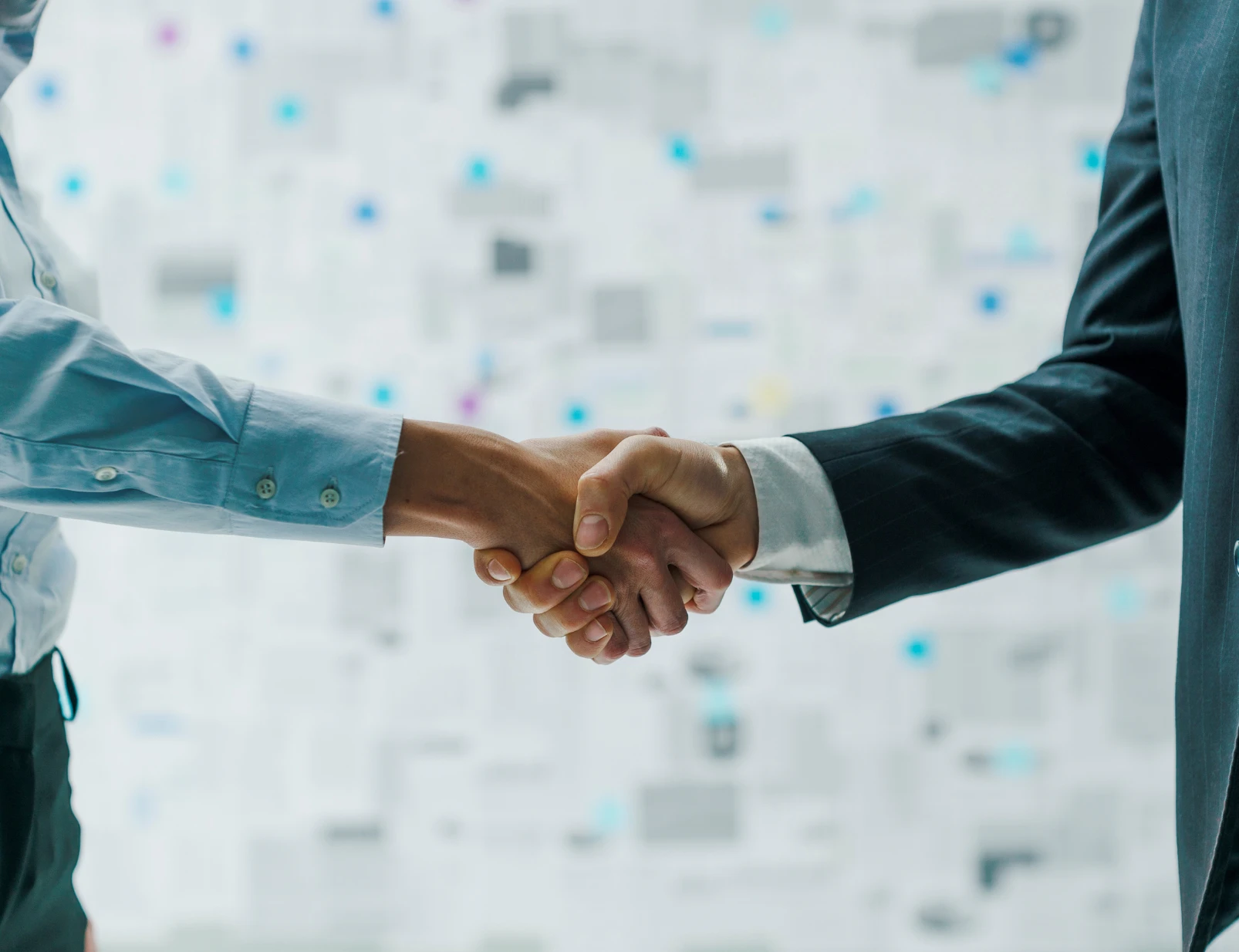 Two men shake hands in front of a wall of squares.