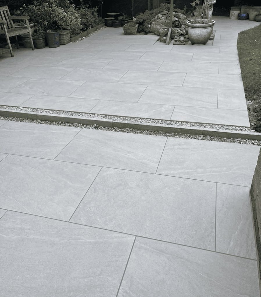 Gray stone patio tiles with a narrow gravel divider and garden pots and benches in the background.