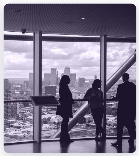 Silhouetten von drei Personen vor einem großen Fenster mit Blick auf eine Stadtlandschaft und Wolken.