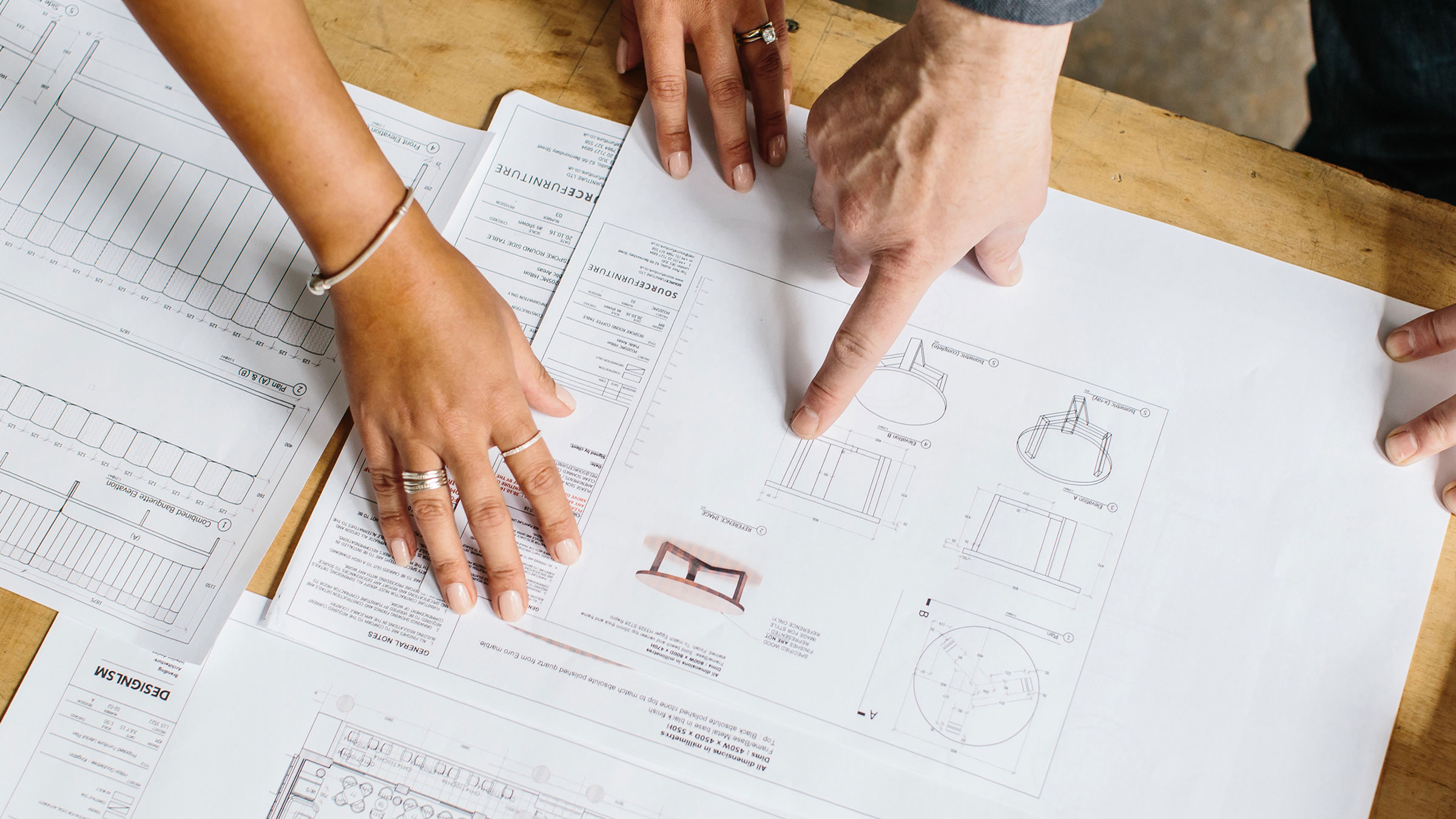Two peoples hands on table technical drawing