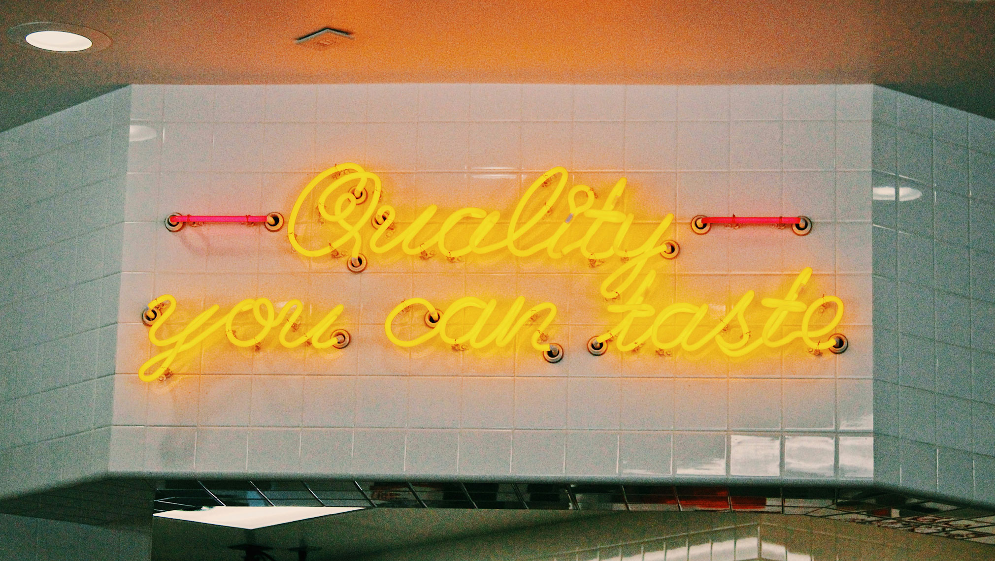 Quality you can taste neon on tiled restaurant wall