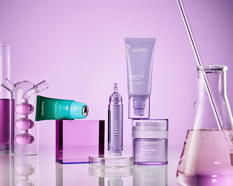 Dr Idriss skincare products displayed with lab glassware on a purple background.