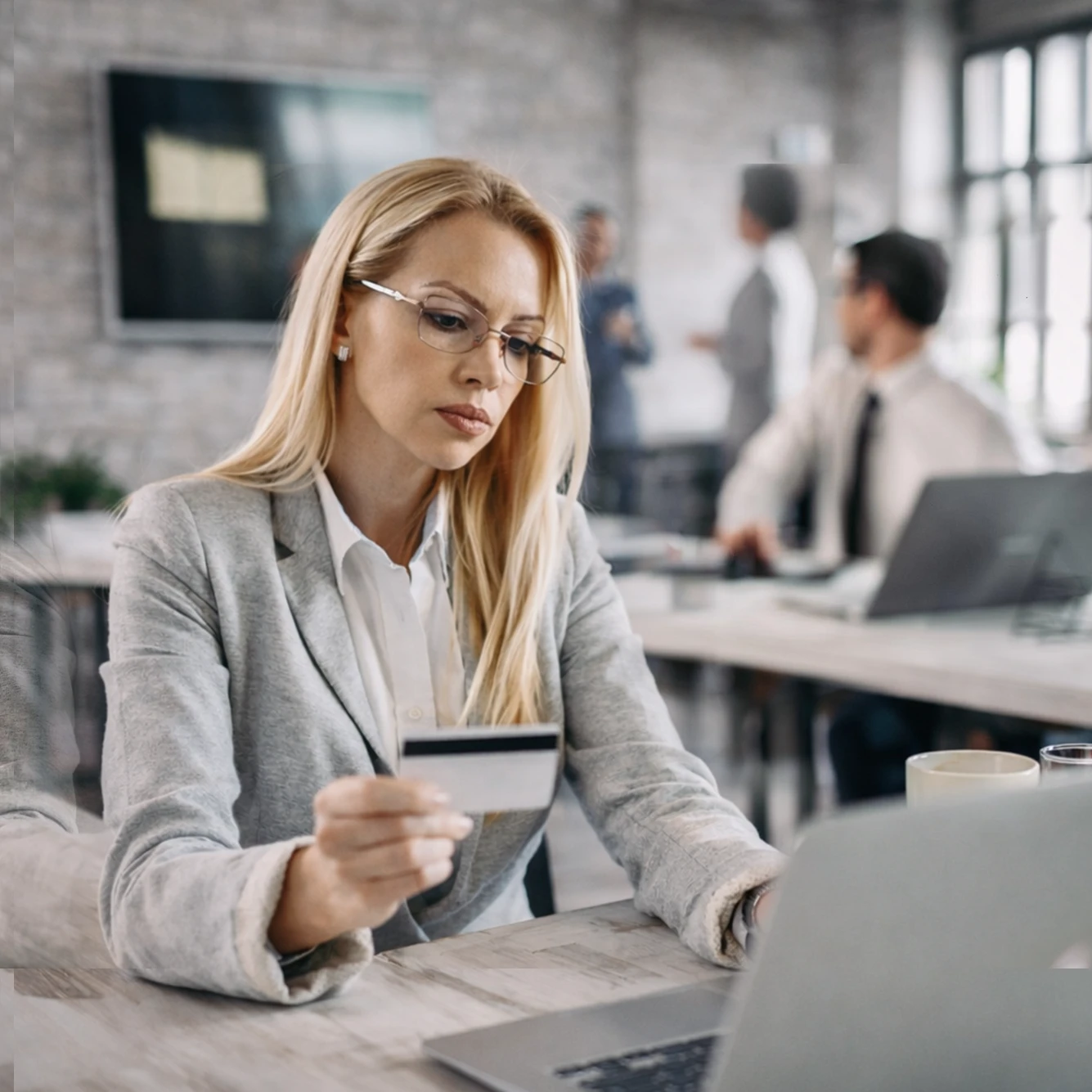 Professional using a credit card while working on a laptop in an office.