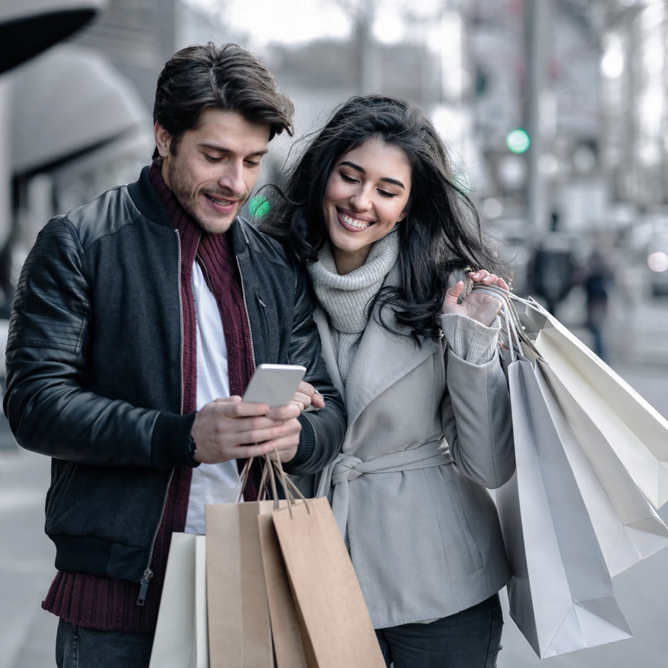 Two people with shopping bags looking at a smartphone together on a city street.