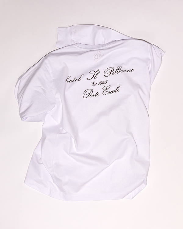 White polo shirt with black script text reading 'hotel Il Pellicano Est. 1965 Porto Ercole' on the back.