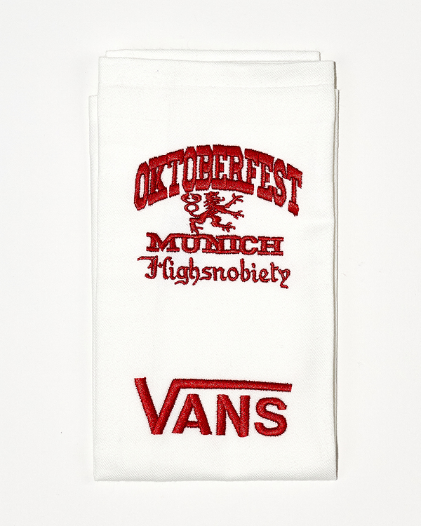 White folded socks with red embroidery reading 'OKTOBERFEST', 'MUNICH', 'Highsnobiety', and the Vans logo.