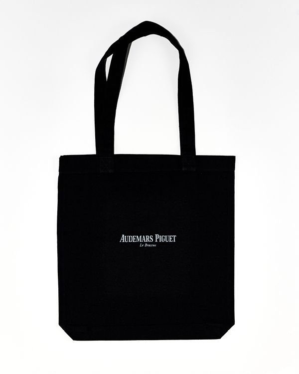 Black tote bag with long handles featuring the text 'Audemars Piguet Le Brassus' printed in white.