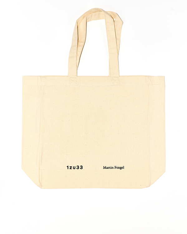 Beige canvas tote bag with two handles, printed with '1zu33' and 'Martin Fengel' in black text on the front.