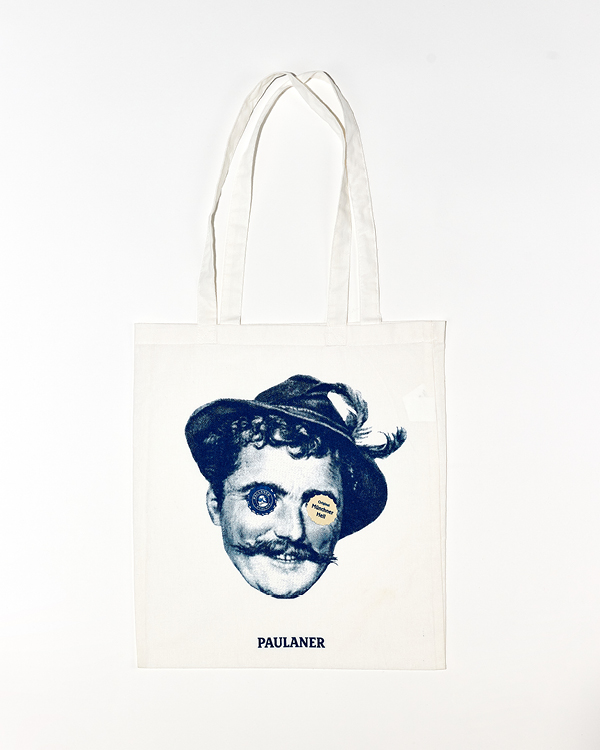 White tote bag featuring a vintage man's face wearing a feathered hat with a button over each eye and 'PAULANER' printed below.