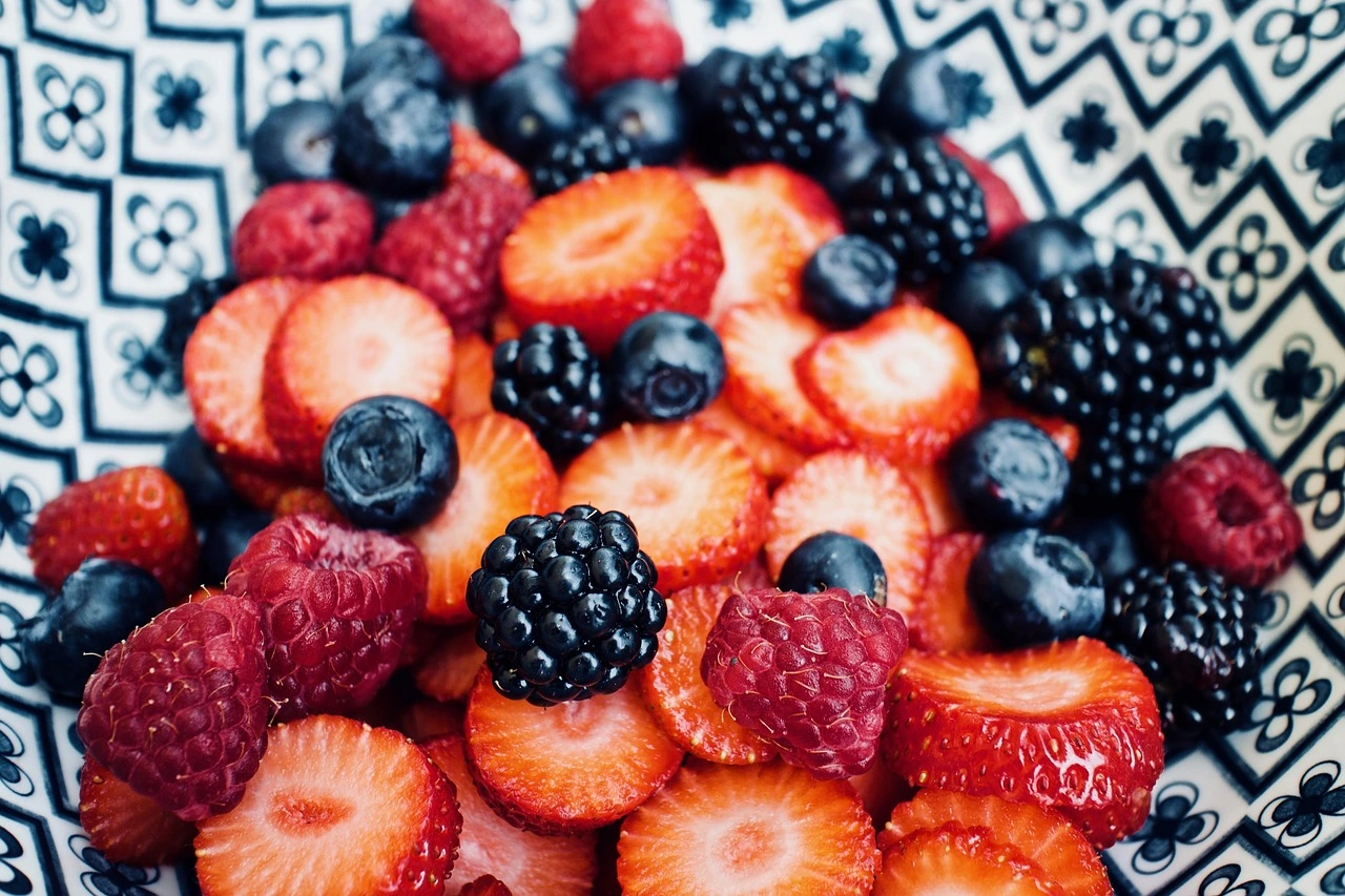 A close-up bowl of mixed berries including sliced strawberries, raspberries, blueberries, and blackberries, served in a patterned dish.