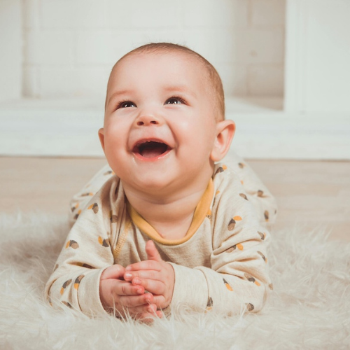 Smiling baby lying on a soft rug in cozy pajamas, looking up with joy and laughter in a warm, softly lit room.