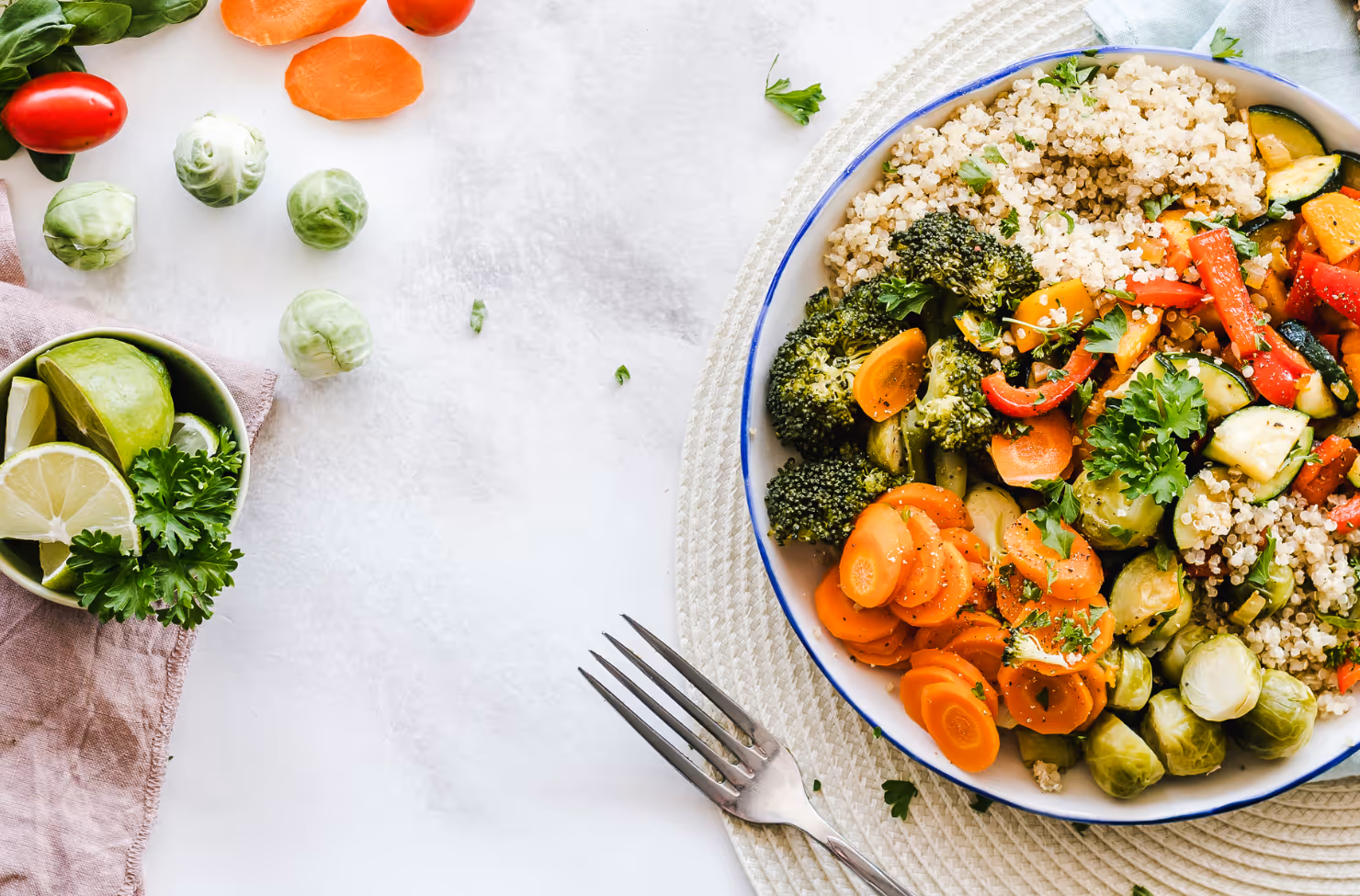 Colorful bowl of quinoa with roasted vegetables including broccoli, carrots, peppers, and Brussels sprouts on white table